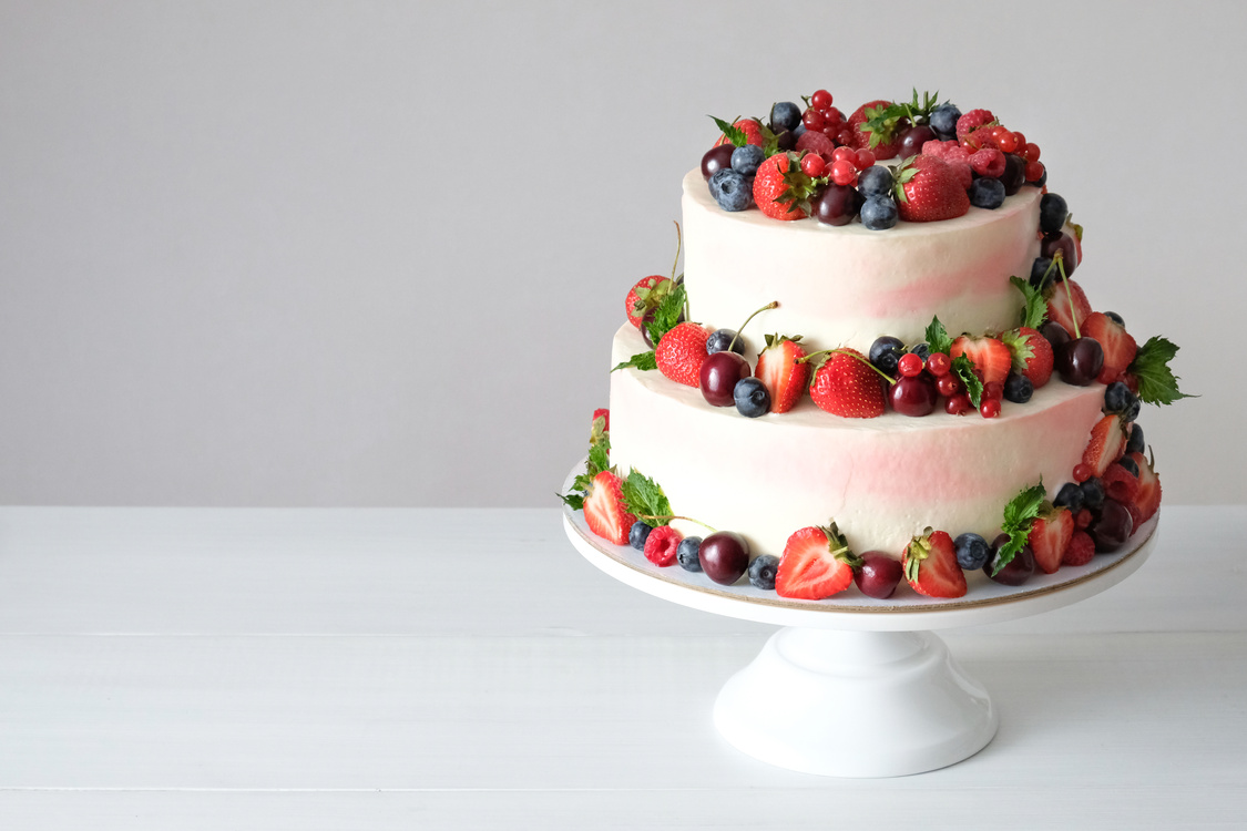 Two-tiered wedding cake in chocolate, with slices strawberries, raspberries, blackberry on a white background.